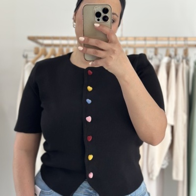 Top preto com botões coloridos de coração sendo usado por pessoa a tirar selfie na loja