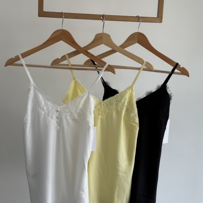 Três camisolas de cetim branco, amarelo e preto com renda em cabides de madeira.