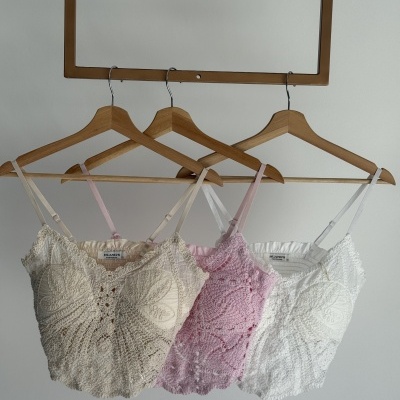 Três tops de renda coloridos pendurados em cabides de madeira