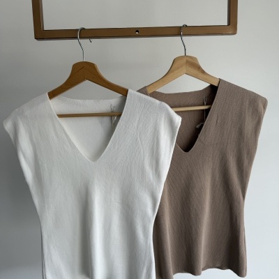 Dois coletes de tecido malha branco e castanho claro pendurados em cabides de madeira