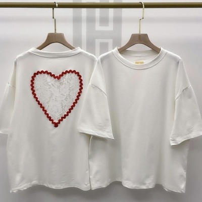 Duas t-shirts brancas, uma com coração de renda vermelha na parte traseira, penduradas em cabides de madeira