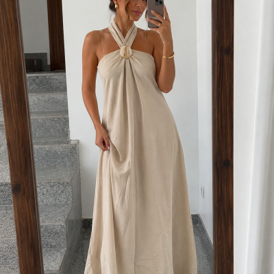 Vestido longo bege com alças cruzadas e fivela circular usado por mulher