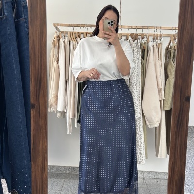 Saia comprida azul escura de pontos brancos e renda na barra, com camiseta branca, vista em espelho de madeira numa loja de roupas.