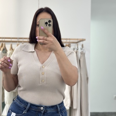 Mulher a usar t-shirt bege de malha com botões dourados e jeans azul escuro com etiqueta MOM FIT