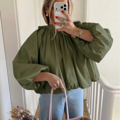 Pessoa com blusa verde, jeans e mala de palha rosa com flores secas, em interior com paredes brancas.