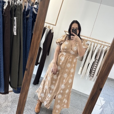 Vestido comprido bege com flores brancas e botas castanhas visto ao espelho numa loja de roupa