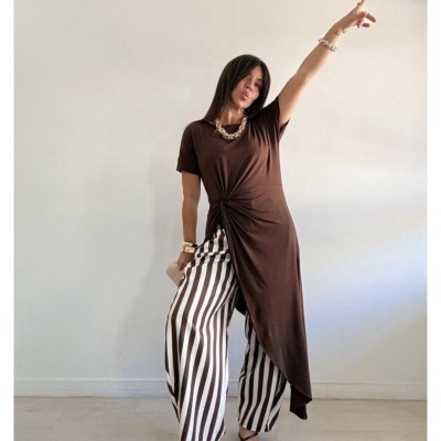 Mulher com roupa castanha e calças riscas numa pose dinâmica
