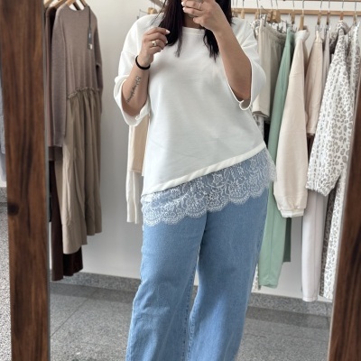 Mulher com blusa branca com renda e calças de ganga azul claro, tirando selfie num espelho