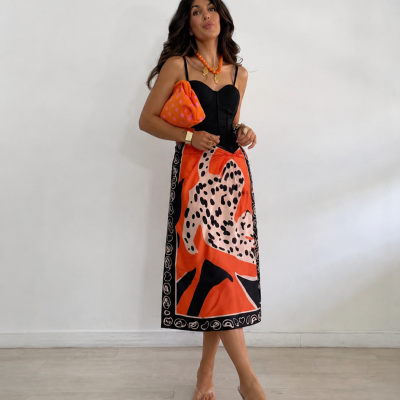 Mulher com vestido comprido preto e roupa com padrão laranja, handbag laranja, colar laranja, fundo branco