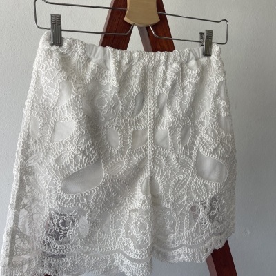 Calção branco de renda com padrão floral em cabide de madeira