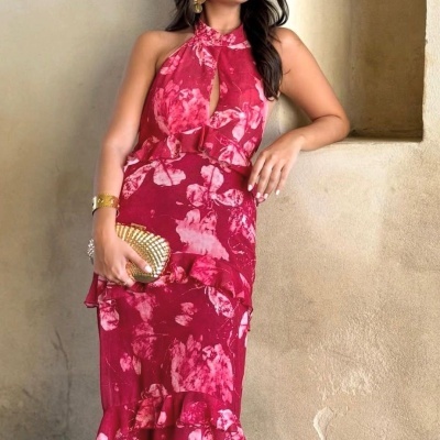 Mulher com vestido longo vermelho floral, mala dourada e acessórios em fundo rústico