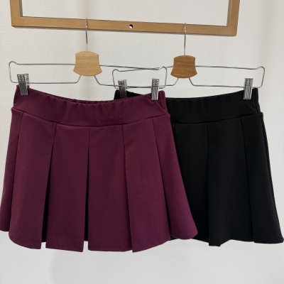 Duas saias plissadas, uma vinho e outra preta, penduradas em cabides de metal com suporte de madeira.