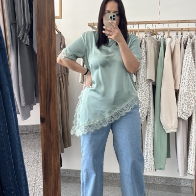 Mulher com blusa verde água e jeans a tirar selfie num espelho