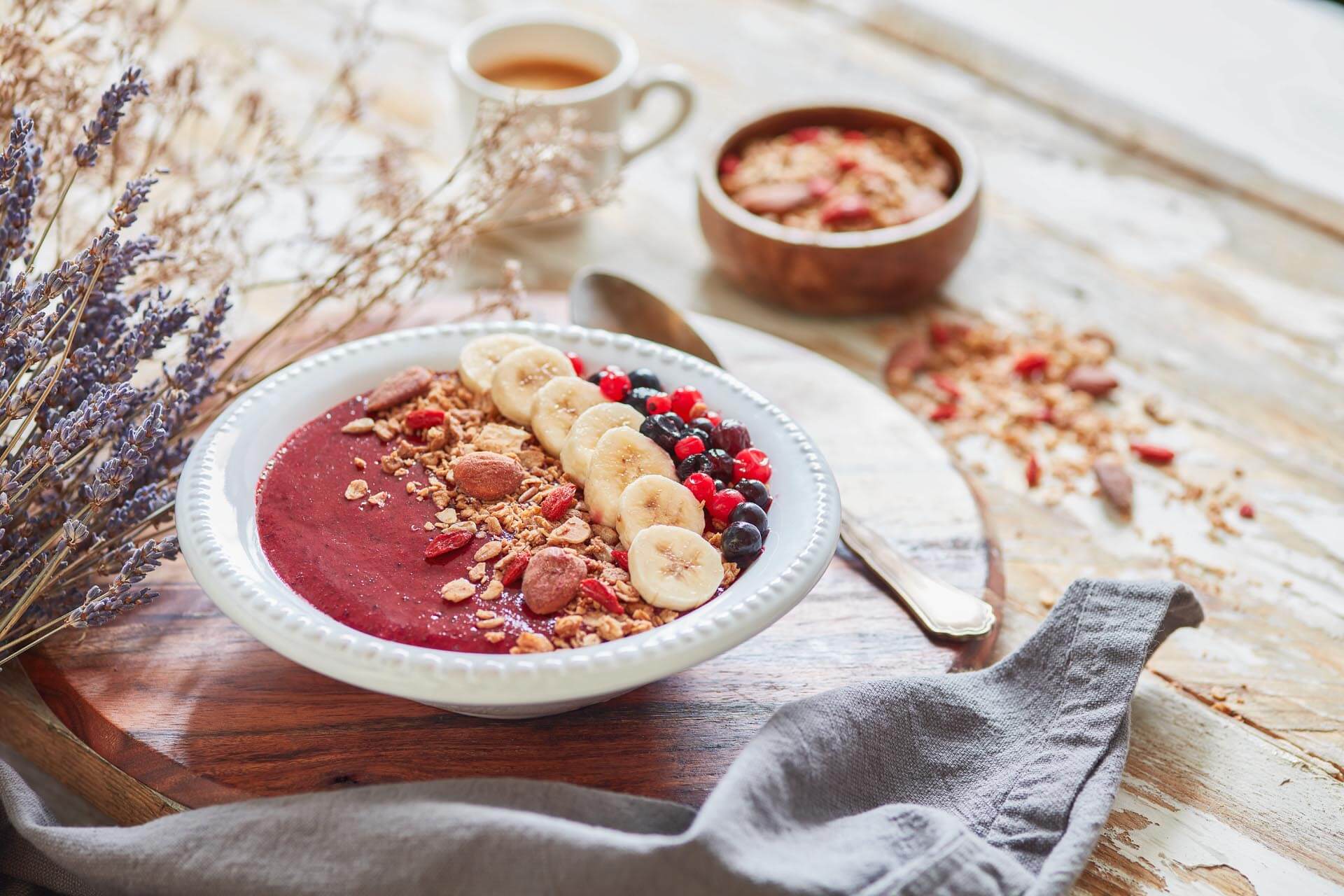 granola goji e amêndoa BIO sem glúten - 1800g Taça branca com smoothie vermelho decorado com fruta e granola numa mesa de madeira