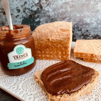 Frasco de creme de avelã Trinca, pão cortado e fatia com creme numa bandeja branca