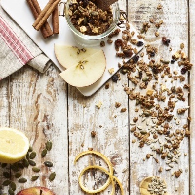 Granola em frasco de vidro, maçã, paus de canela, sementes e limão sobre madeira rústica