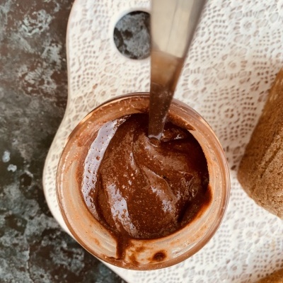 Frasco com creme castanho escuro e colher numa tábua branca rendilhada