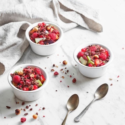 Sobremesas em taças brancas com frutas frescas, frutos secos e pedaços de chocolate numa mesa de mármore branca