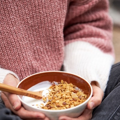 Pessoa a segurar tigela com iogurte e granola, usa camisola rosa e branca