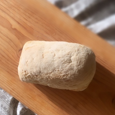 Pão rústico claro sobre tábua de madeira com pano estampado ao fundo e texto sobreposto.