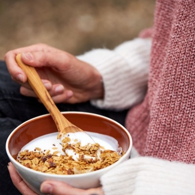 Pessoa a segurar tigela de iogurte com granola e colher de madeira