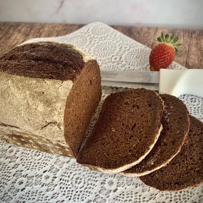 Pão de côdea escura fatiado em toalha de renda branca com morango ao fundo