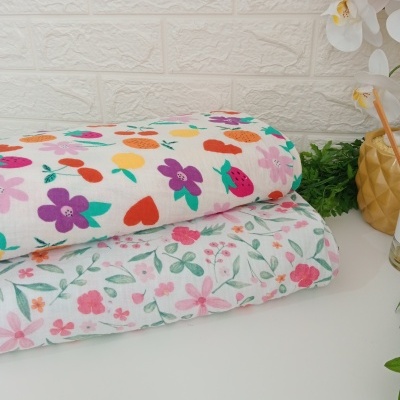 Mantas o toallas de tela con estampados florales coloridos en una mesa blanca junto a plantas y una pared blanca texturizada