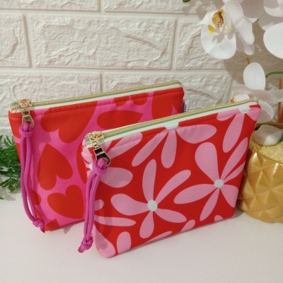 Dos neceseres coloridos con diseño de flores y corazones sobre fondo blanco con plantas decorativas