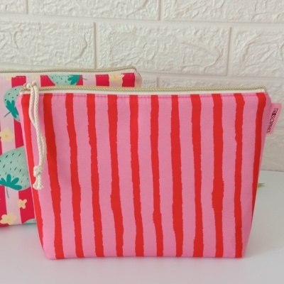 Bolsas de tela con cierre, una con rayas rojas y rosas y otra con fresas sobre fondo rosa frente a pared blanca texturizada