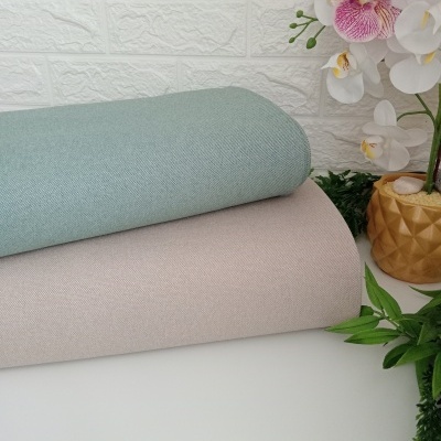 Dos rollos de tela azul claro y beige sobre mesa blanca con fondo blanco y flores a la derecha