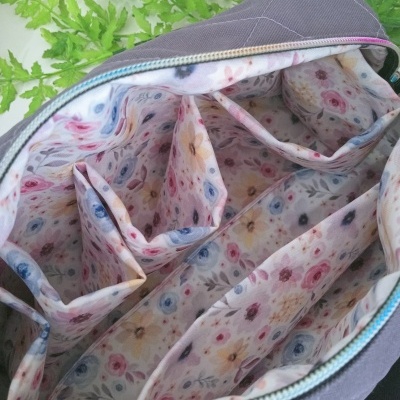 Interior de bolsa cinza com forro floral colorido e múltiplos compartimentos