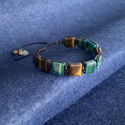 Pulseira com pedras castanho e verde em cordão preto sobre tecido azul