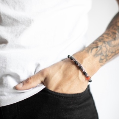 Pessoa com pulseira de contas pretas e vermelha, tatuagem no braço, roupa branca e preta