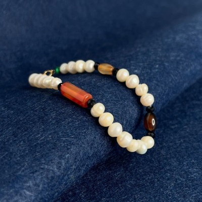 Pulseira com contas de pérola e contas alongadas vermelhas e castanhas sobre tecido azul escuro