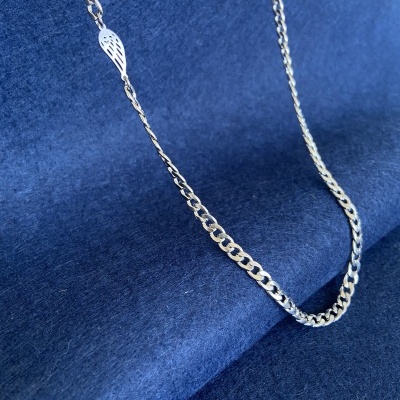 Colar prateado com corrente grossa e pendant em forma de asa sobre fundo azul.
