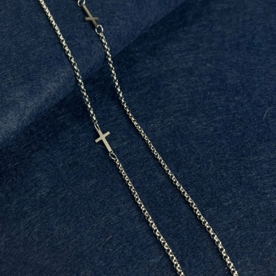 Colar prateado com cruzes sobre tecido azul escuro