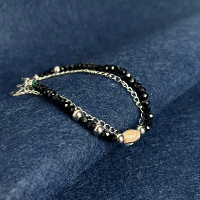 Pulseira com contas pretas, esferas metálicas e conta central bege sobre tecido azul