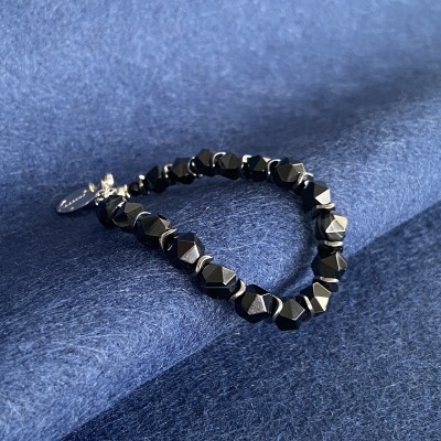 Pulseira preta facetada com fecho prateado sobre tecido azul