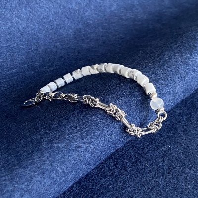 Pulseira com pedras brancas e corrente metálica sobre tecido azul escuro