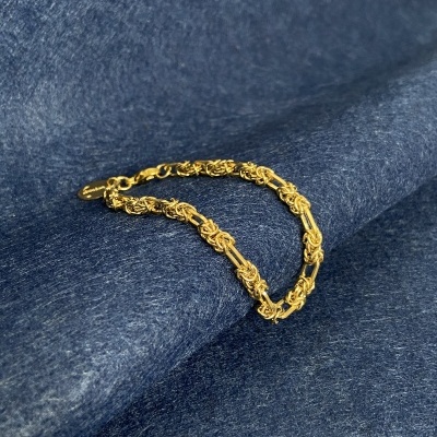 Pulseira dourada entrelaçada sobre tecido azul