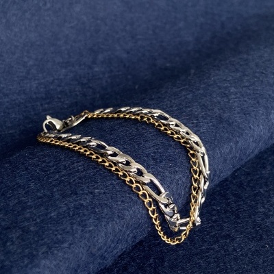 Pulseira com correntes prateada e dourada sobre tecido azul escuro