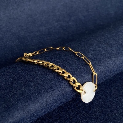 Pulseira dourada com disco branco sobre tecido azul escuro