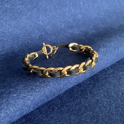 Pulseira dourada e preta com fecho toggle sobre tecido azul.