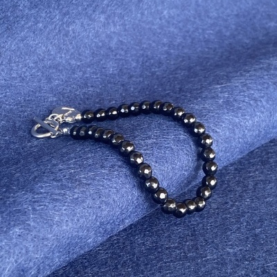 Pulseira de contas pretas espelhadas com fecho metálico sobre tecido azul