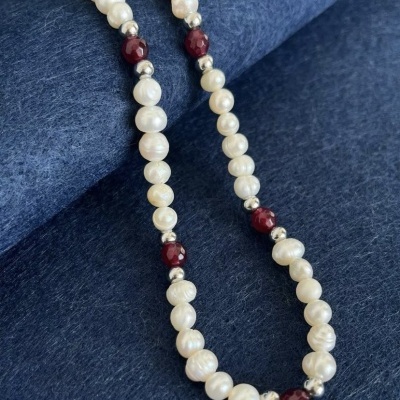 Colar de pérolas brancas com contas metálicas prateadas e bordô sobre tecido azul.