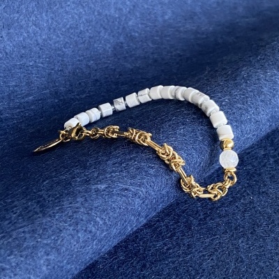 Pulseira de miçangas brancas e corrente dourada sobre tecido azul escuro