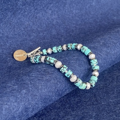 Pulseira de contas azul turquesa e cinza com fecho prateado sobre tecido azul