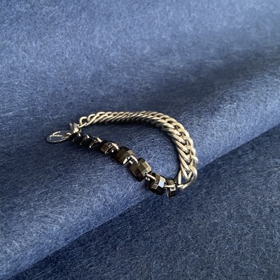 Pulseira de corrente metálica prateada com elos pretos em fundo de tecido cinza azulado