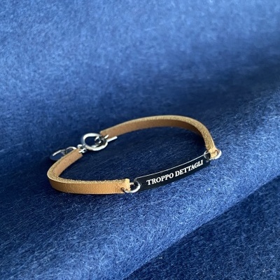 Pulseira castanha com placa preta e texto branco sobre tecido azul