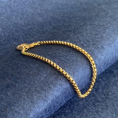 Pulseira dourada de elos quadrados sobre tecido azul
